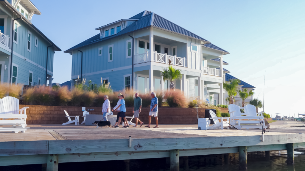 People walking along a wooden dock by light blue waterfront vacation homes.