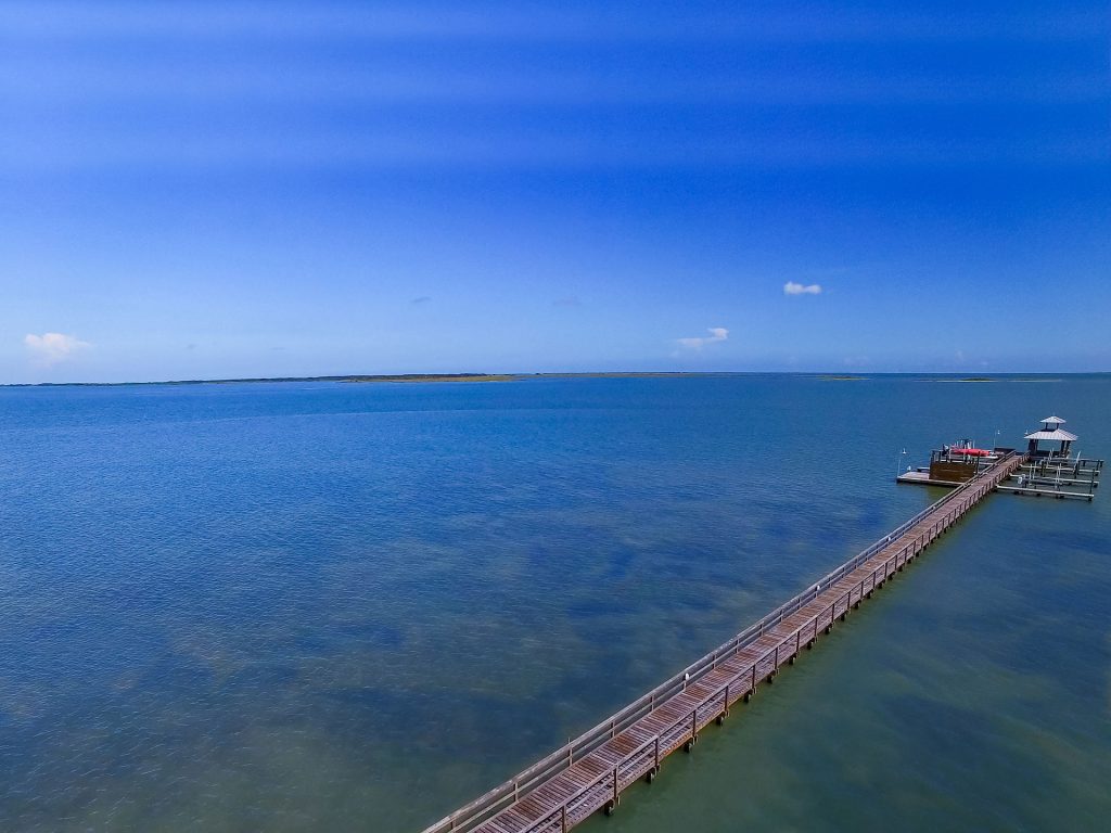 Long wooden pier with a gazebo extending into calm blue water.
