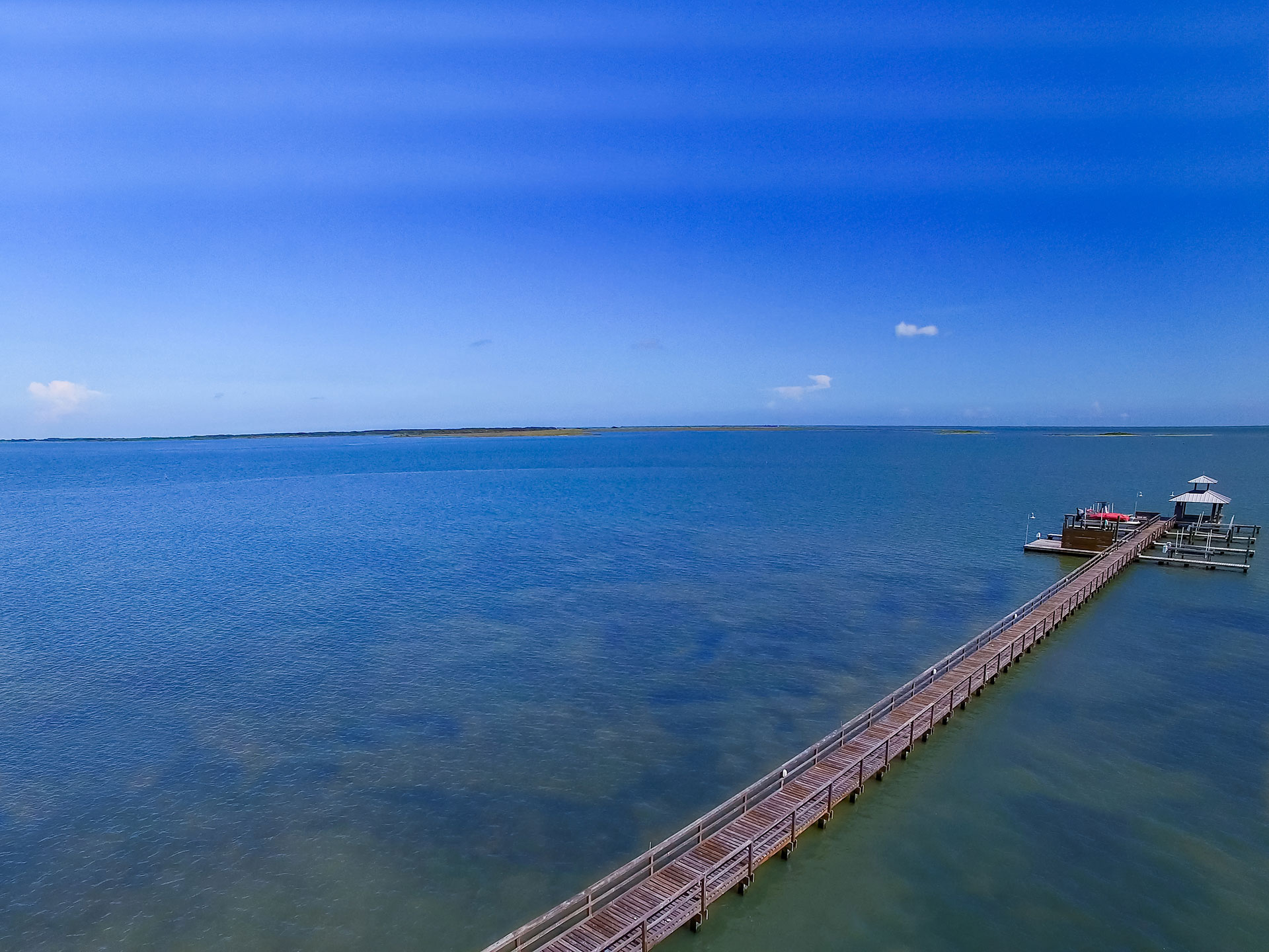 Long wooden pier with a gazebo extending into calm blue water.