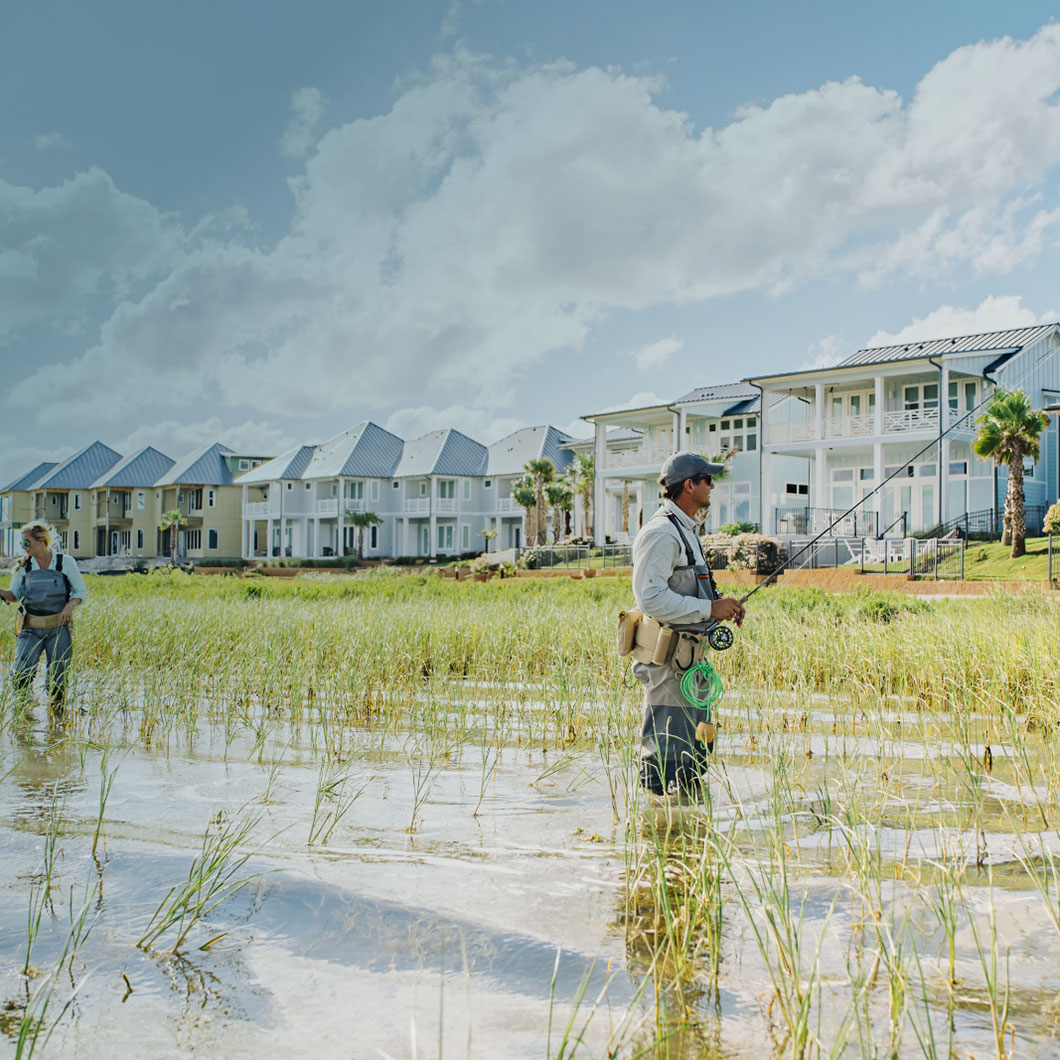 Fly fishing in a coastal marsh with modern waterfront villas in the background.