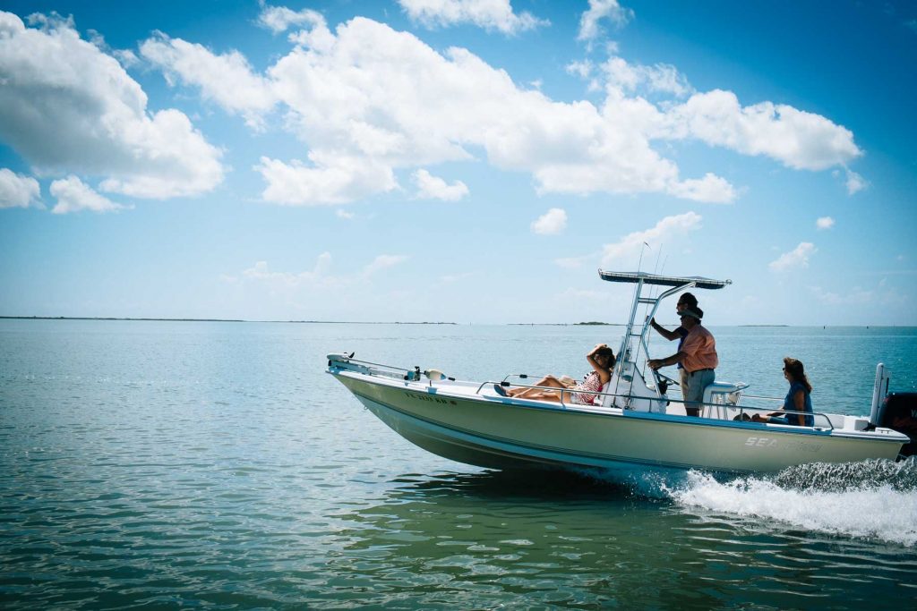 Sea Pro motorboat cruising across calm blue water with people on a sunny day.
