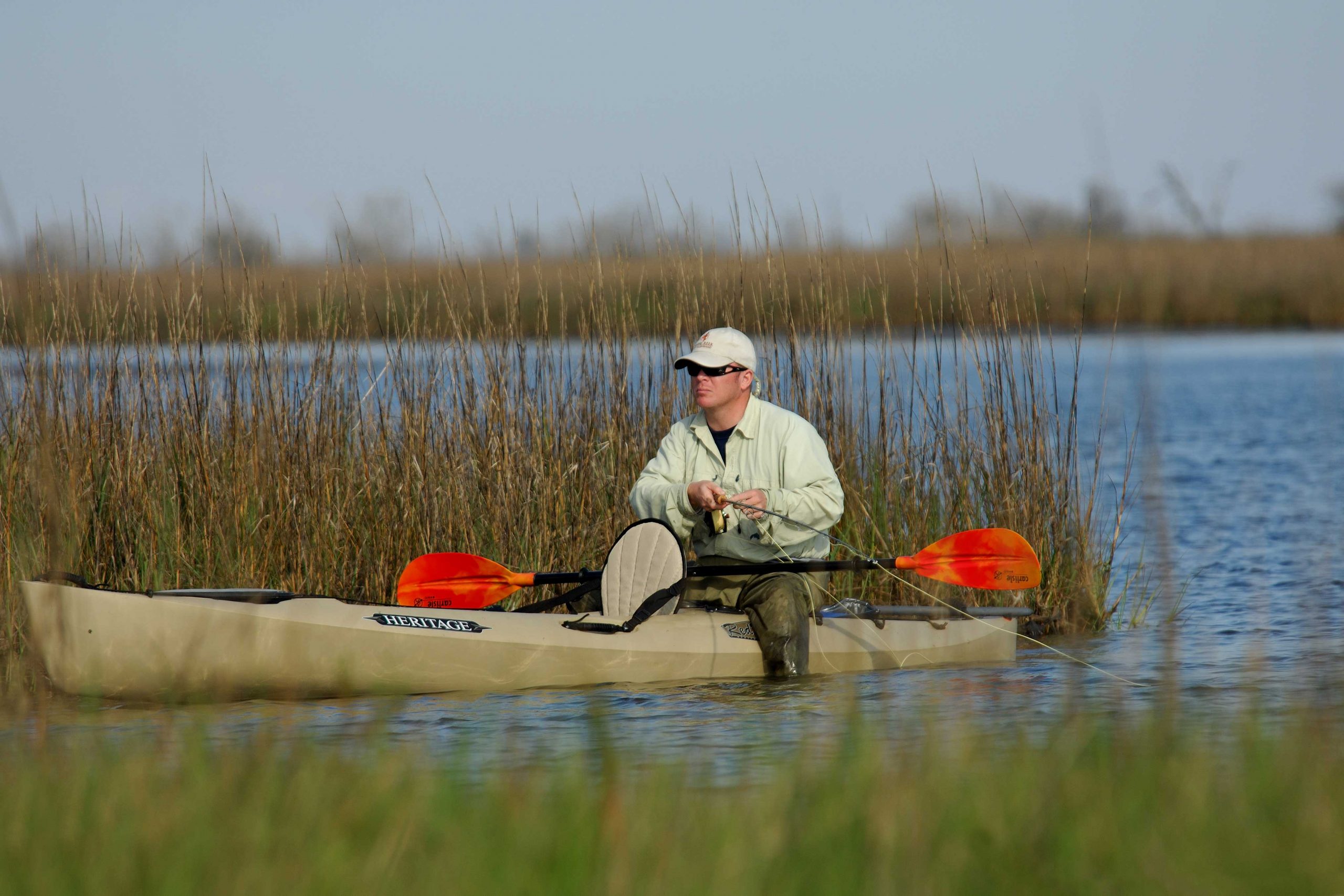 Angler fly fishing from a Heritage kayak in a grassy marsh.