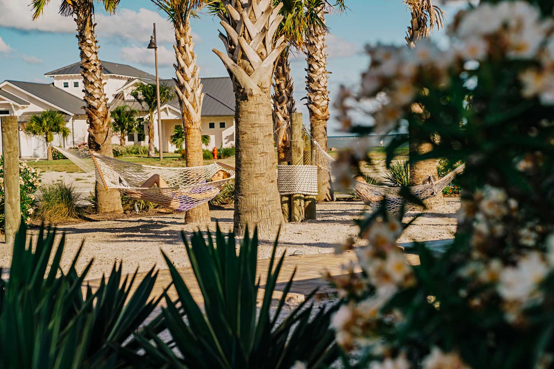 Woman relaxing in a rope hammock between palm trees at a coastal resort.