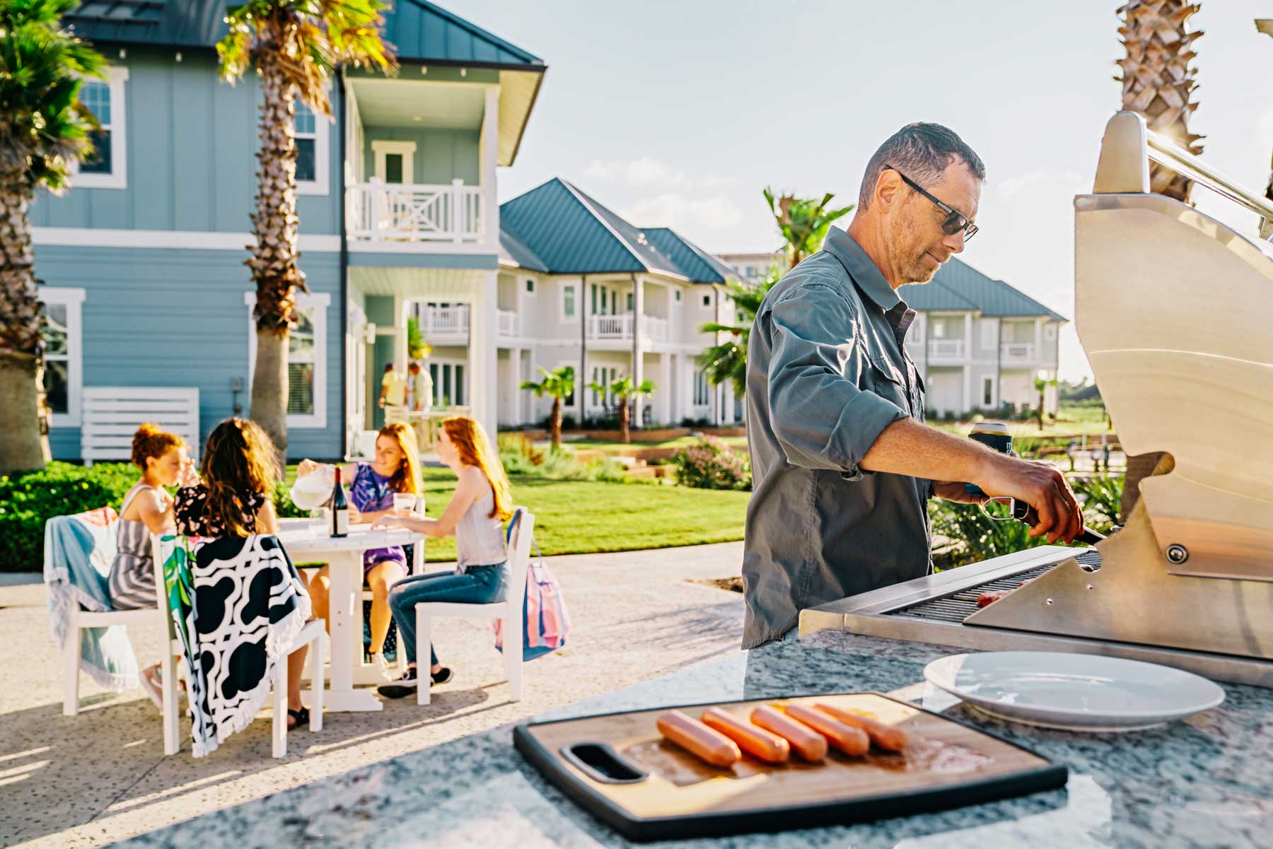 Man grilling hot dogs for friends at a sunny coastal vacation resort.