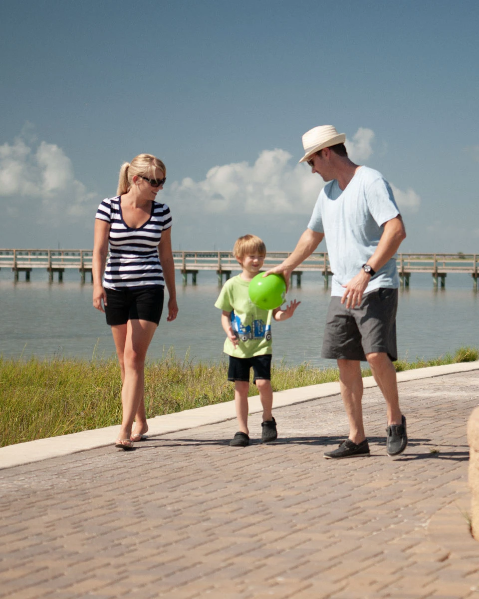 Family walking on a waterfront path while playing with a green ball.